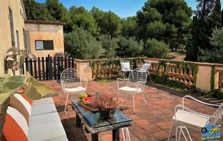 View from a room at Masia Can Casadellà overlooking another terrace with lounge seating, surrounded by olive groves, woods, and cypress trees